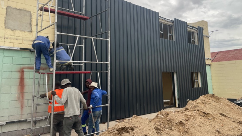 Workers on scaffolding installing black external cladding.