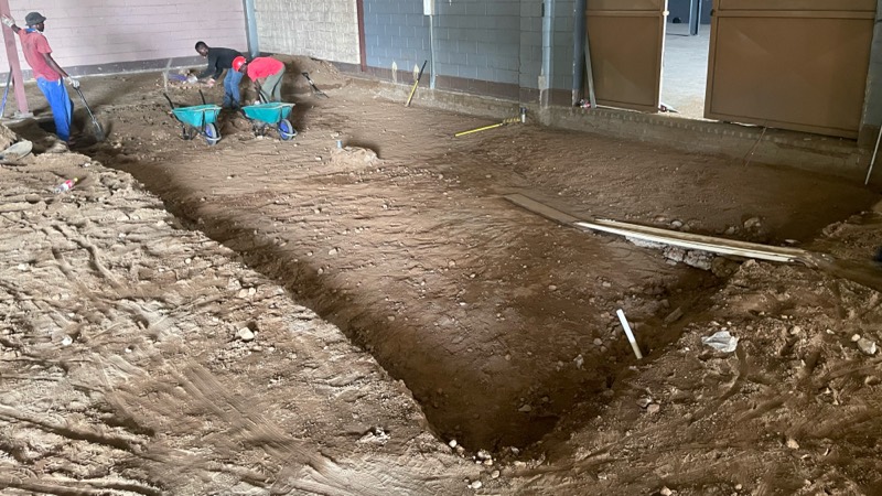 Workers digging foundations inside the building, with excavated earth around the trench.