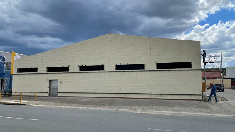 The long existing street facade under a cloudy sky before recladding.