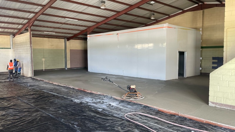 Workers power-floating the new concrete floor beside the finished cold room.