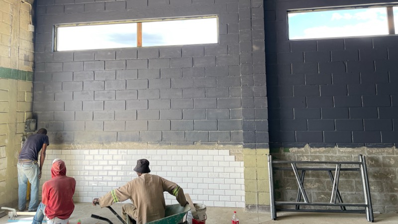 Workers building blockwork and white tiling along an internal wall below new windows.