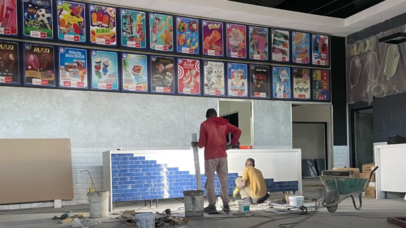 A worker tiling the retail counter below a run of illuminated product panels.