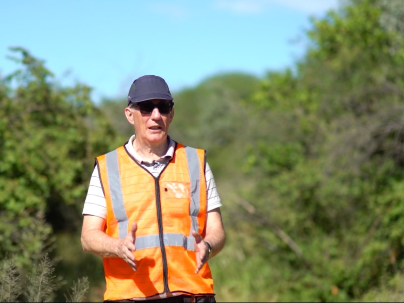 An interviewee in a cap and safety vest speaking on location.
